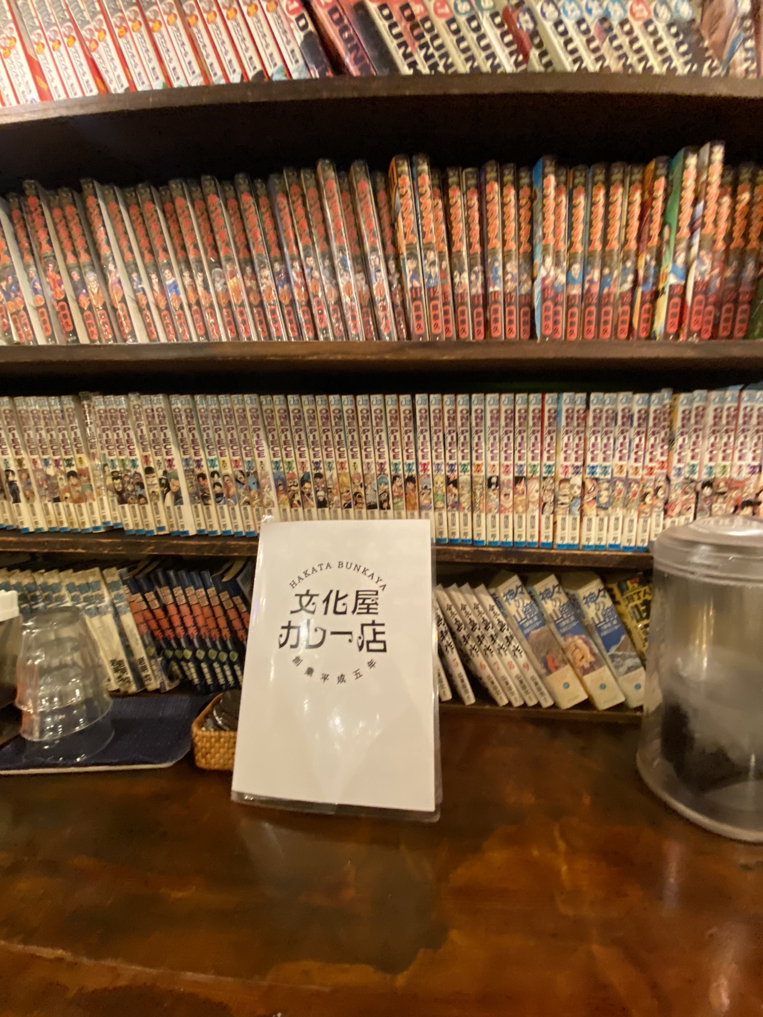文化屋カレー店の内装。壁一面に漫画本が並んだ本棚があり、テーブルにメニューが置かれている
