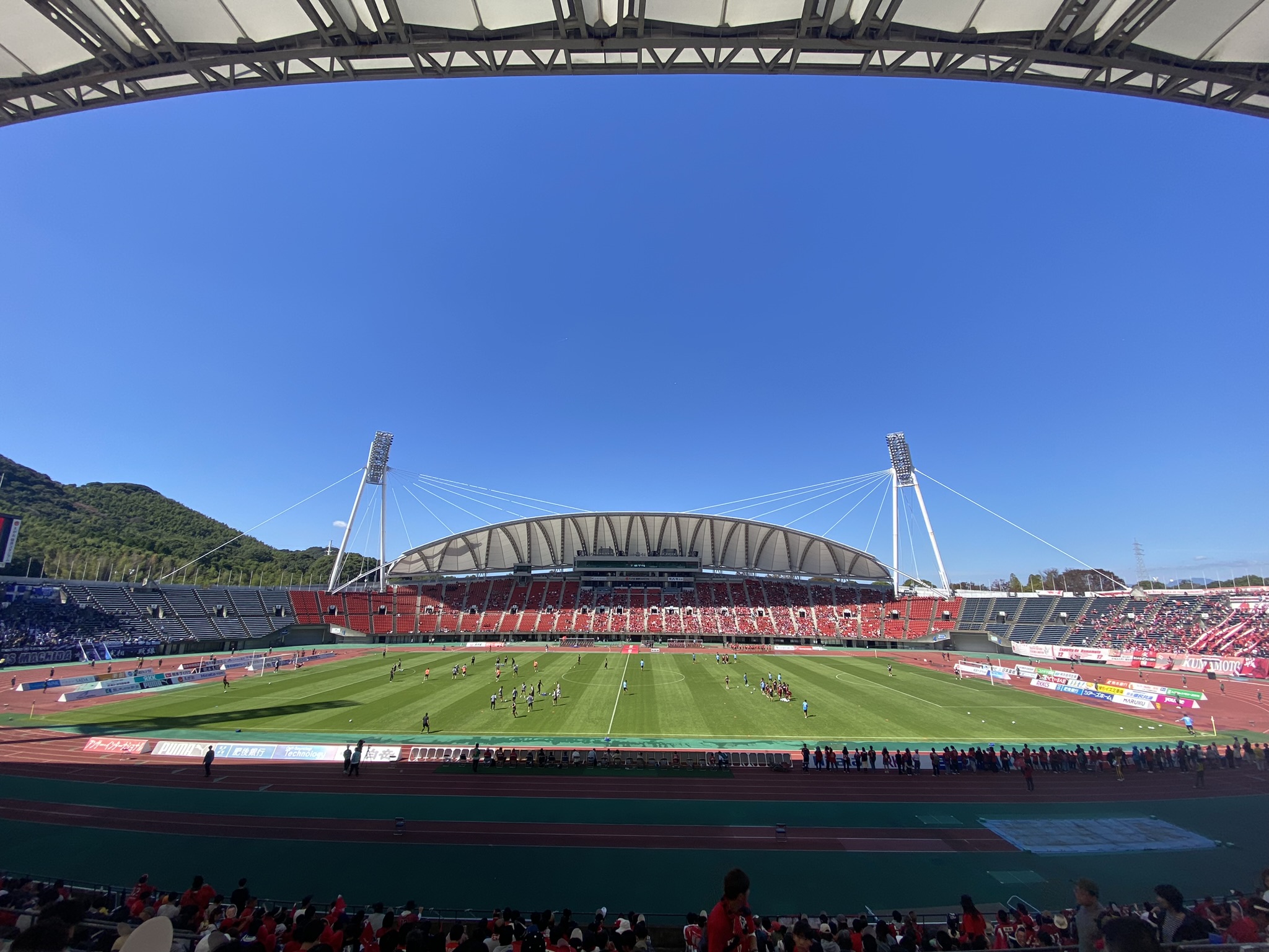 Egao Kenkou Stadium Kumamoto full pitch view under blue sky with mountains in background