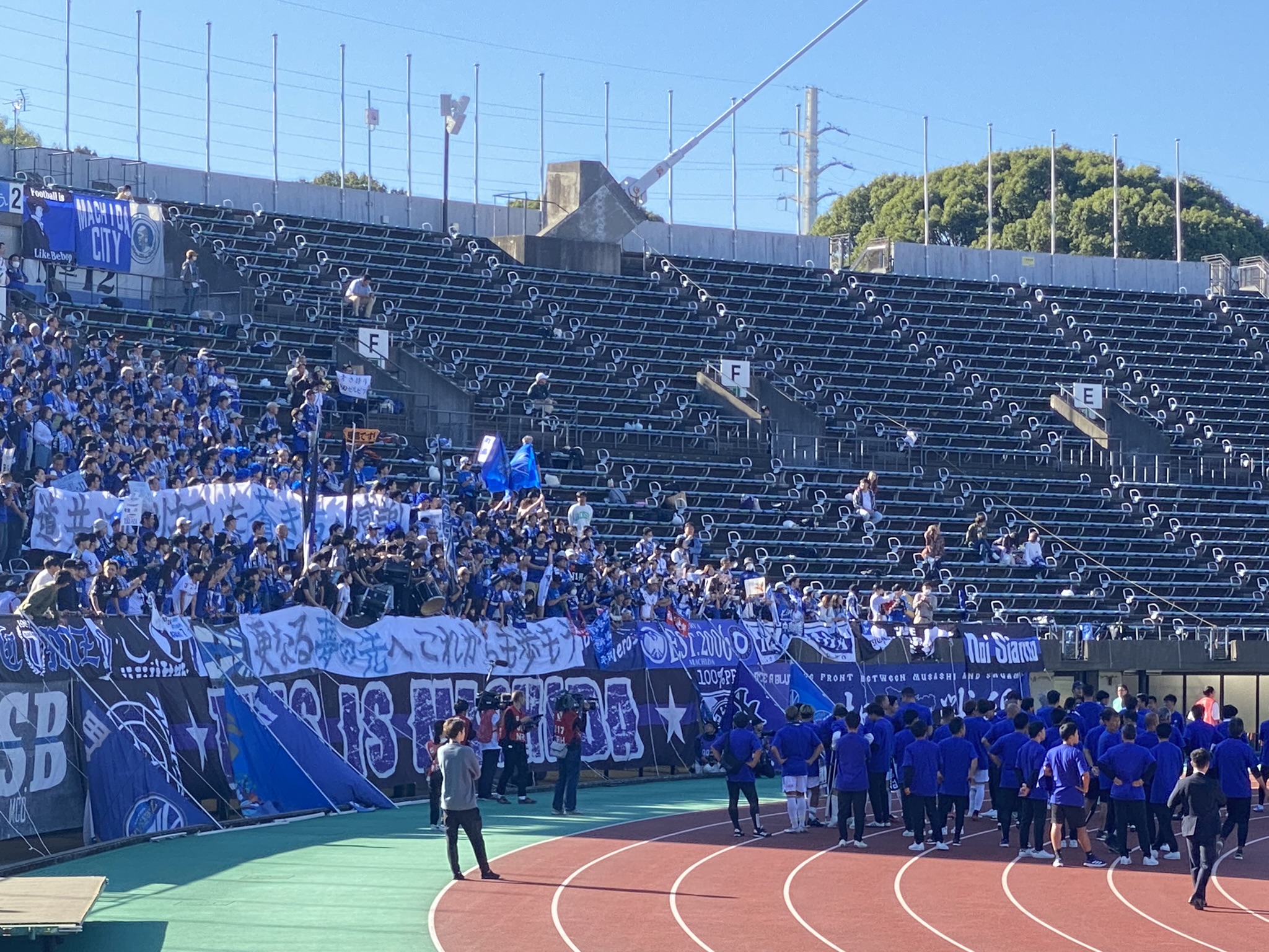 FC Machida Zelvia blue supporter section at Egao Kenkou Stadium with banners and flags