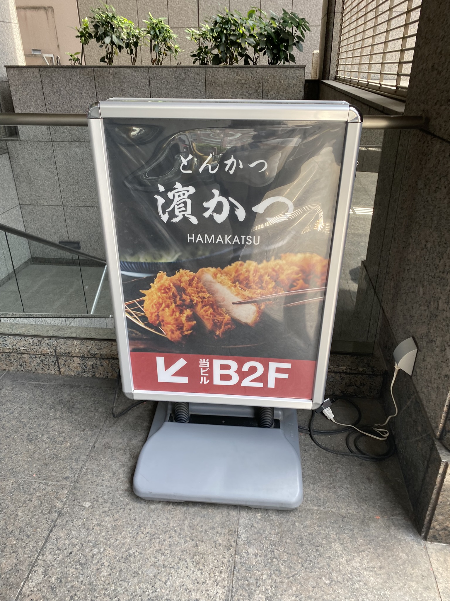 とんかつ濱かつの縦型看板。「どんかつ 濱かつ HAMAKATSU」と書かれ「B2F」の矢印が付いている
