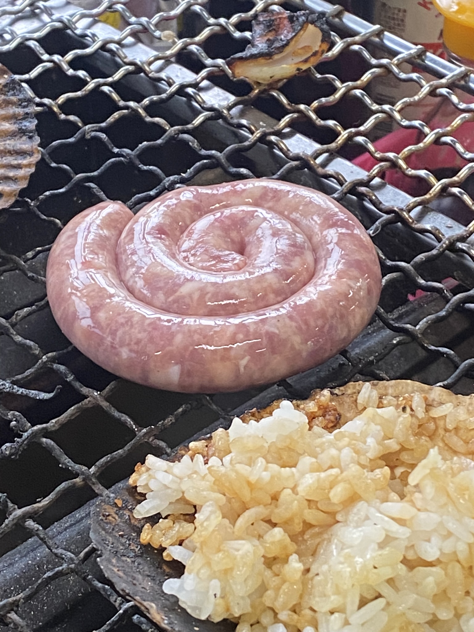 渦巻き状のソーセージが鉄板で焼かれている。横にご飯も