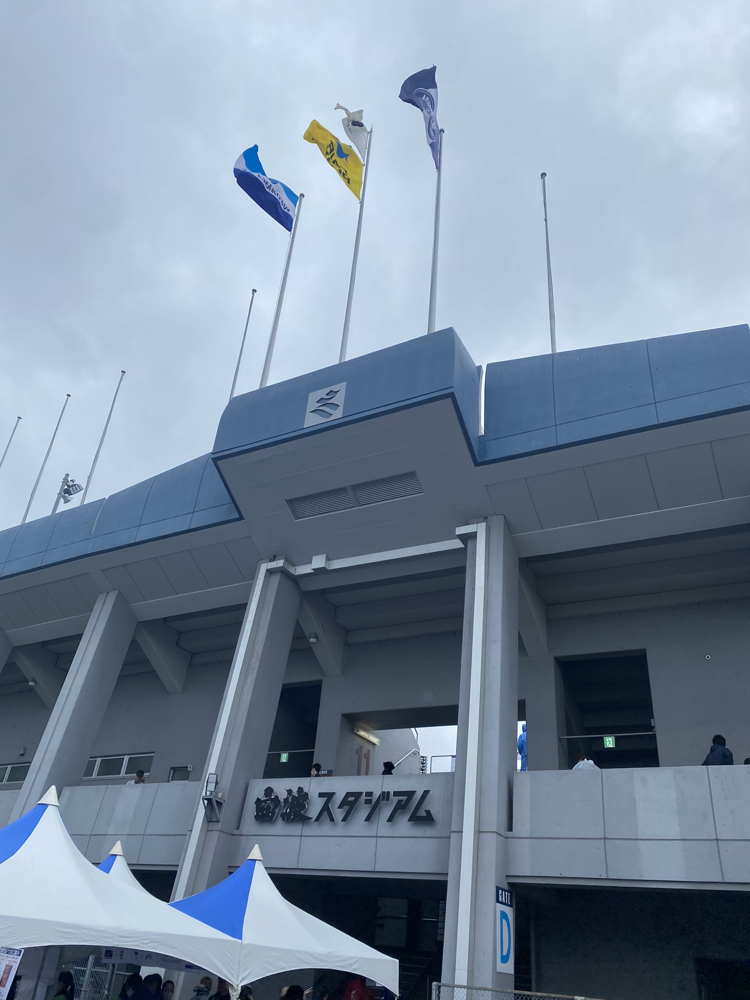 Shiranami Stadium exterior entrance with club flags on mast Kagoshima United FC match day