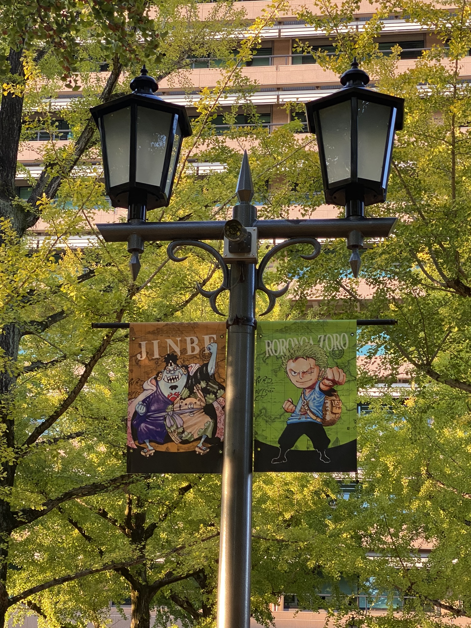 Street lamp banners showing One Piece characters Jinbe and Roronoa Zoro in Kumamoto city
