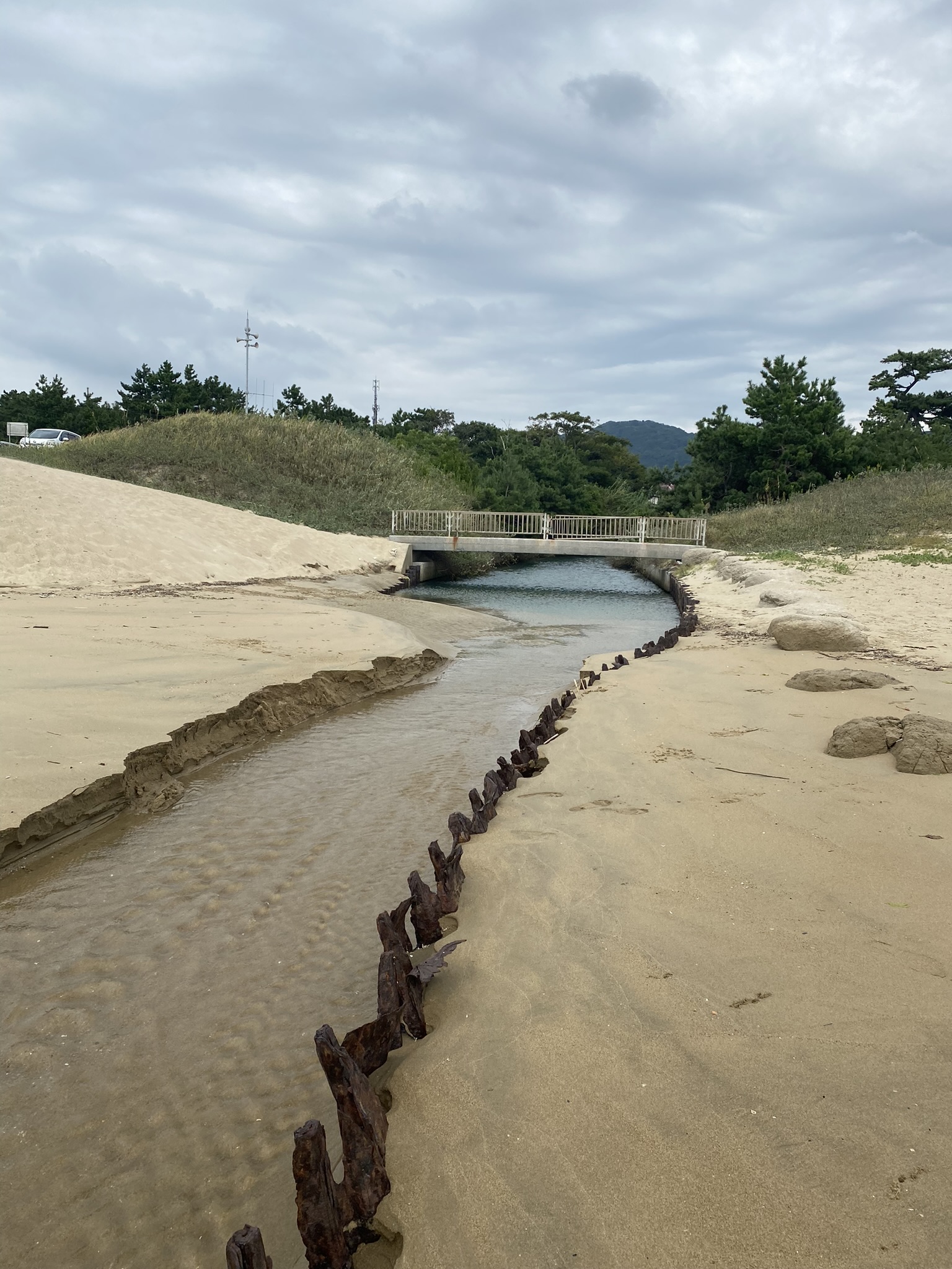 Miyajidake beach Fukuma sandy shore small river stream flowing under bridge wooden posts