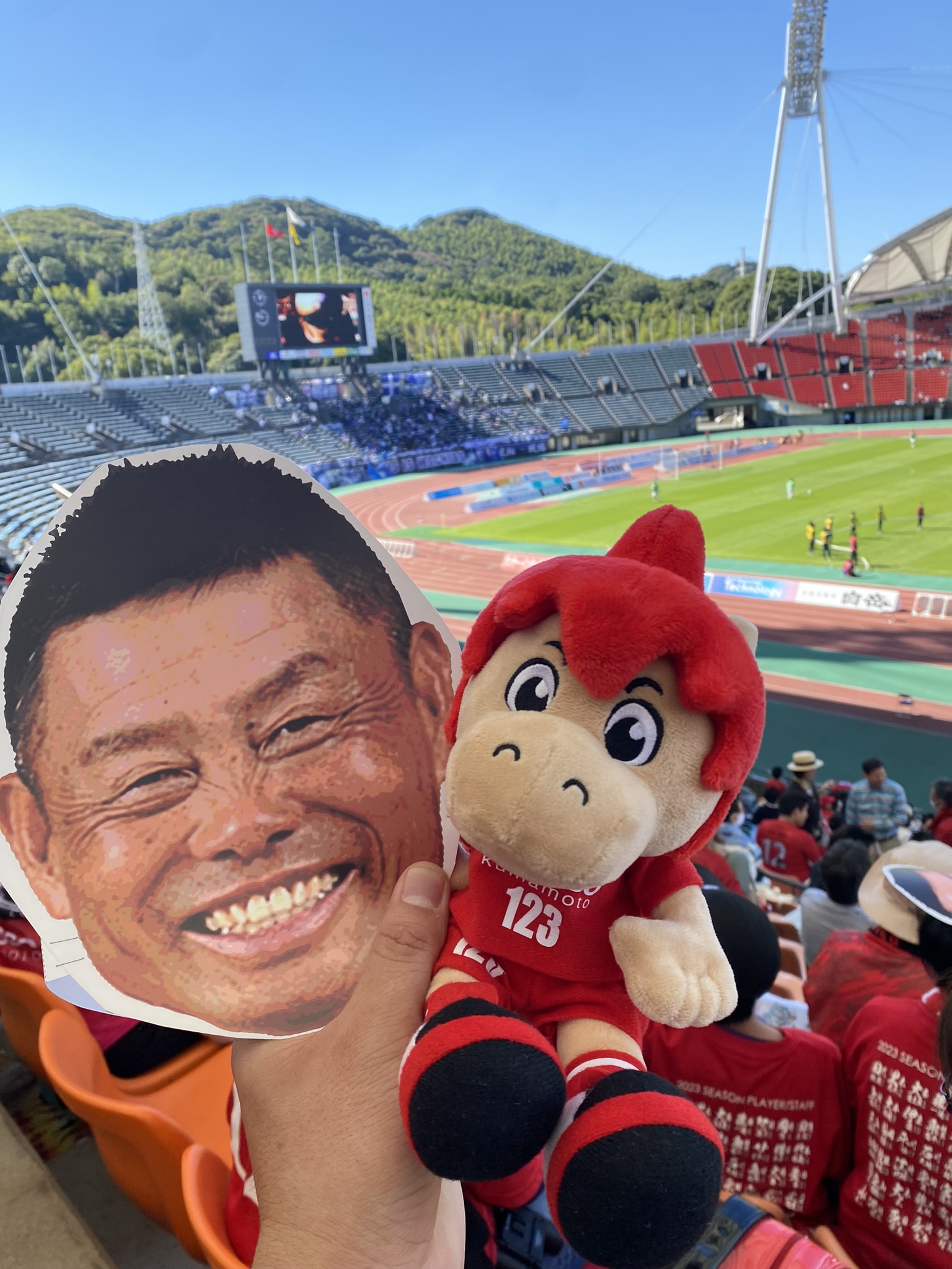 Roasso Kumamoto mascot plush toy and fan holding kumamons face cheerleader board at stadium