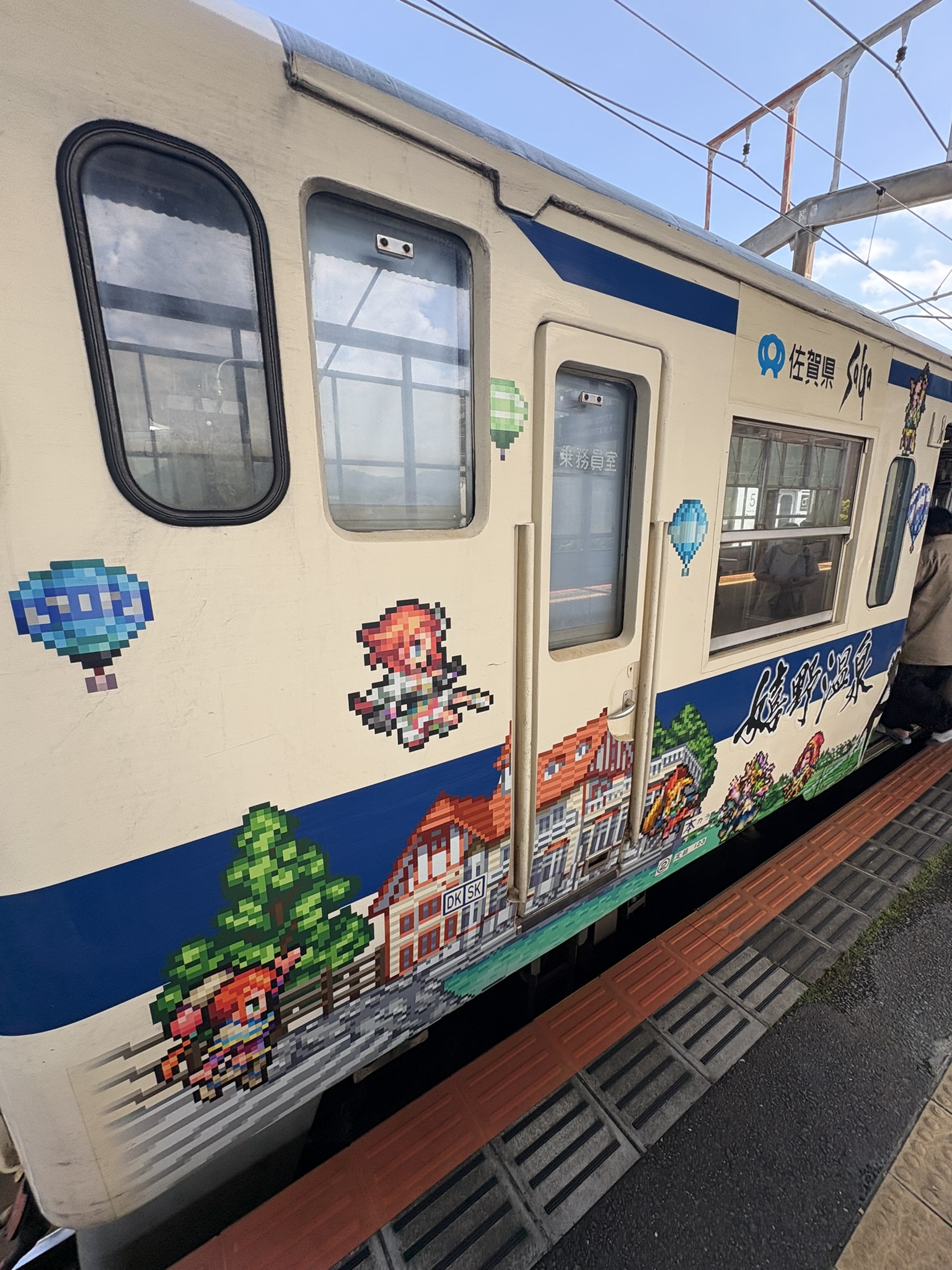 ロマンシング佐賀電車の側面。ドット絵キャラクターと城下町風のイラスト