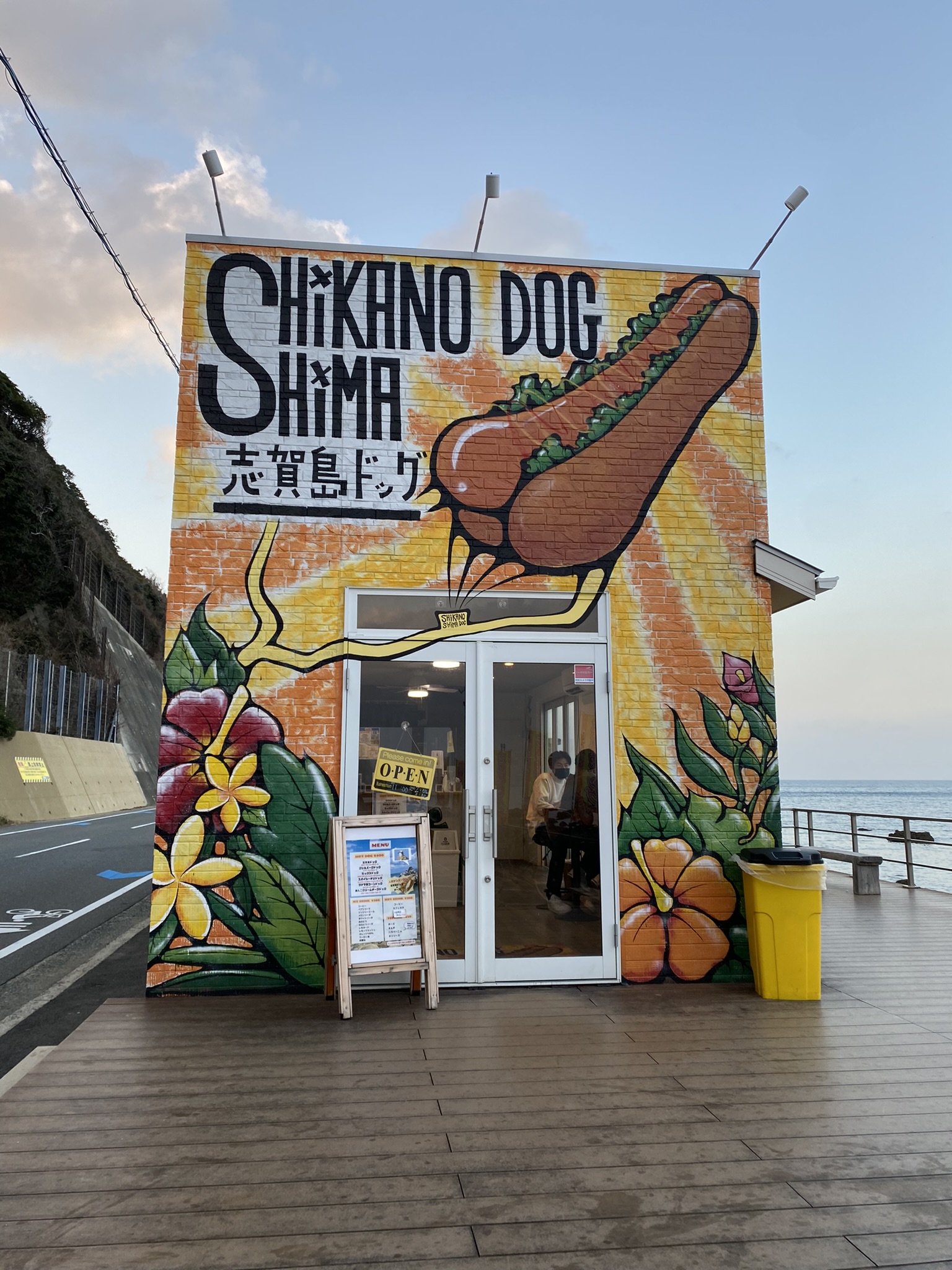 Shikano Dog Shima hotdog shop exterior with colorful wall art and flowers