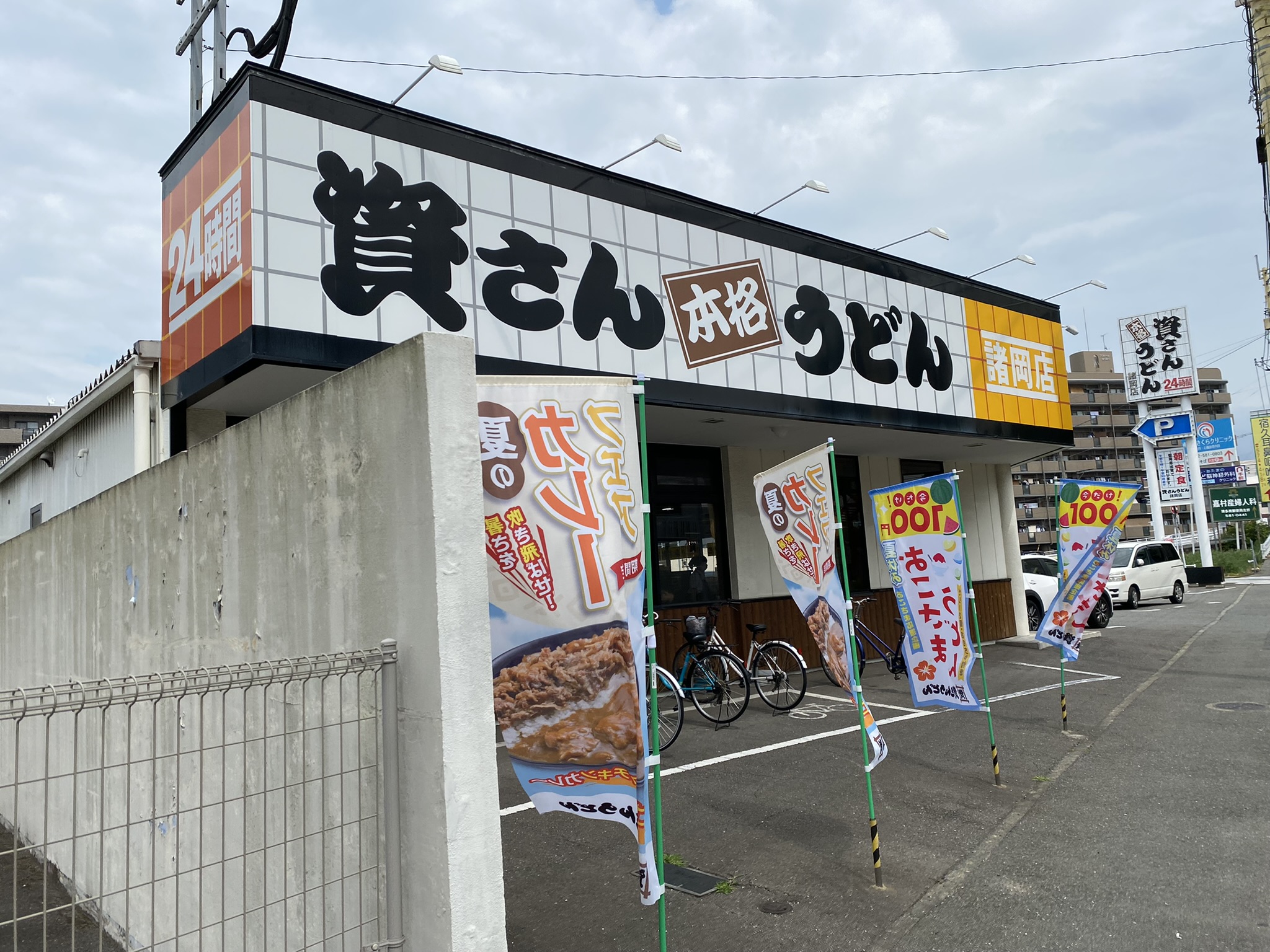 資さんうどんの外観。「賢さん 本格うどん」の大きな看板、24時間営業の文字。駐車場完備の郊外型店舗